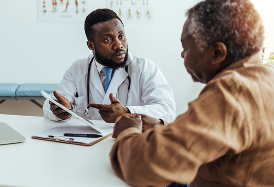 Male health care provider talking to a male patient while sitting at a table.