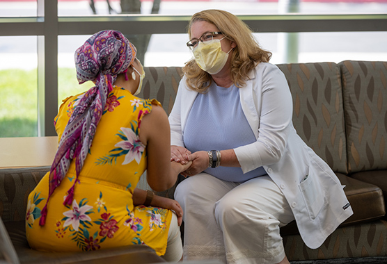 A physician wearing a mask holding the hand of a patient in a multicolored head scarf.
