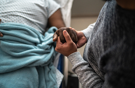 Close-up of a male patient in a hospital bed holding hands with a loved one.