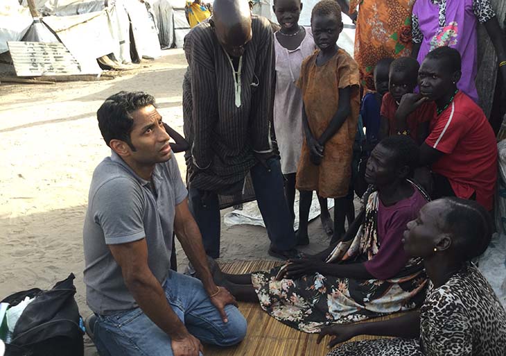 Pranav Shetty kneeling on ground surrounded by Sudanese community members
