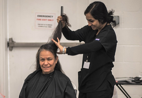 A woman seated on the left receives a haircut from a volunteer on right at a previous Willow Clinic Veterans Day Health Fair