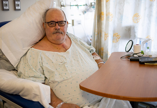 Man sitting in chair wearing hospital gown and scar down his chest