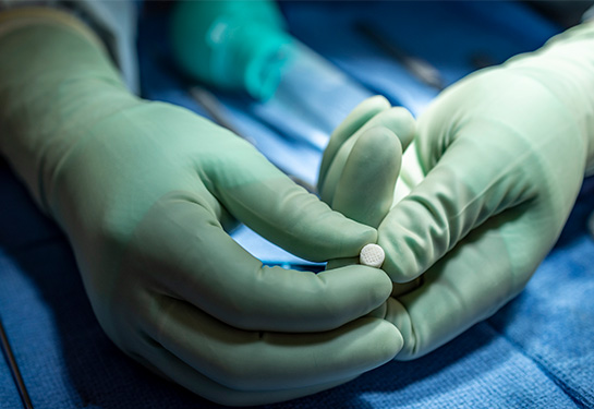 A surgeon holds the small, white cork-shaped CartiHeal implant in her gloved hands.