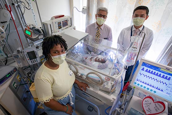 Doctors and parents pose with newborn baby on pediatric bed.