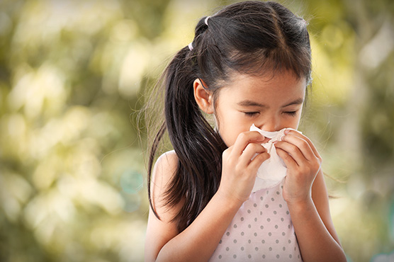 Young girl sneezing outdoors.
