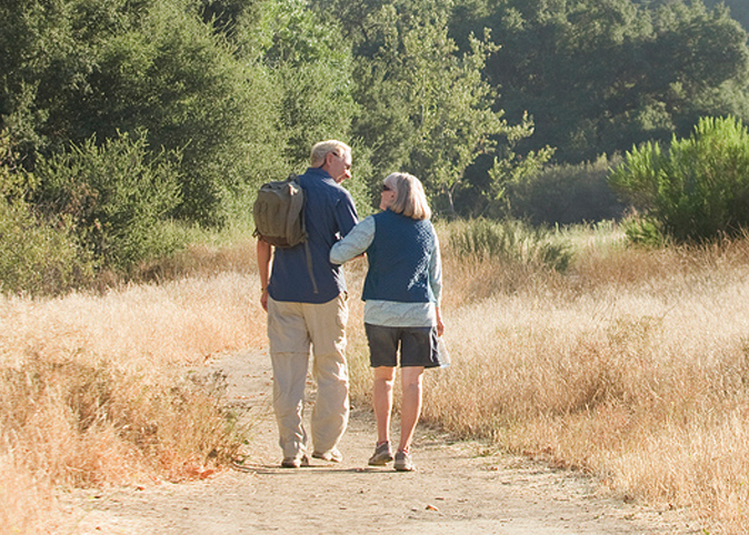 A couple, hiking on a dirt road towards mountains.