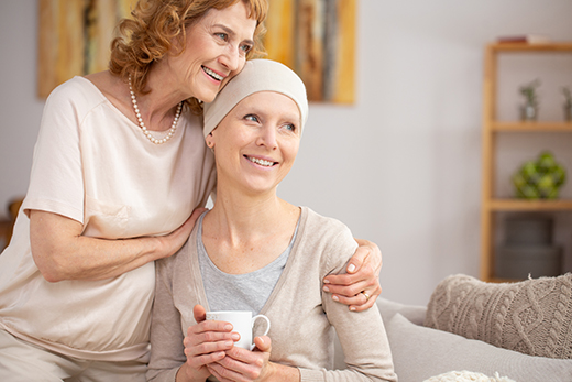 Woman hugging another woman going through cancer treatment, both are smiling