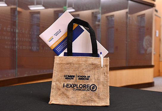 A commemorative handbag made of burlap with the UC Davis School of Medicine I-EXPLORE logo sits on a table